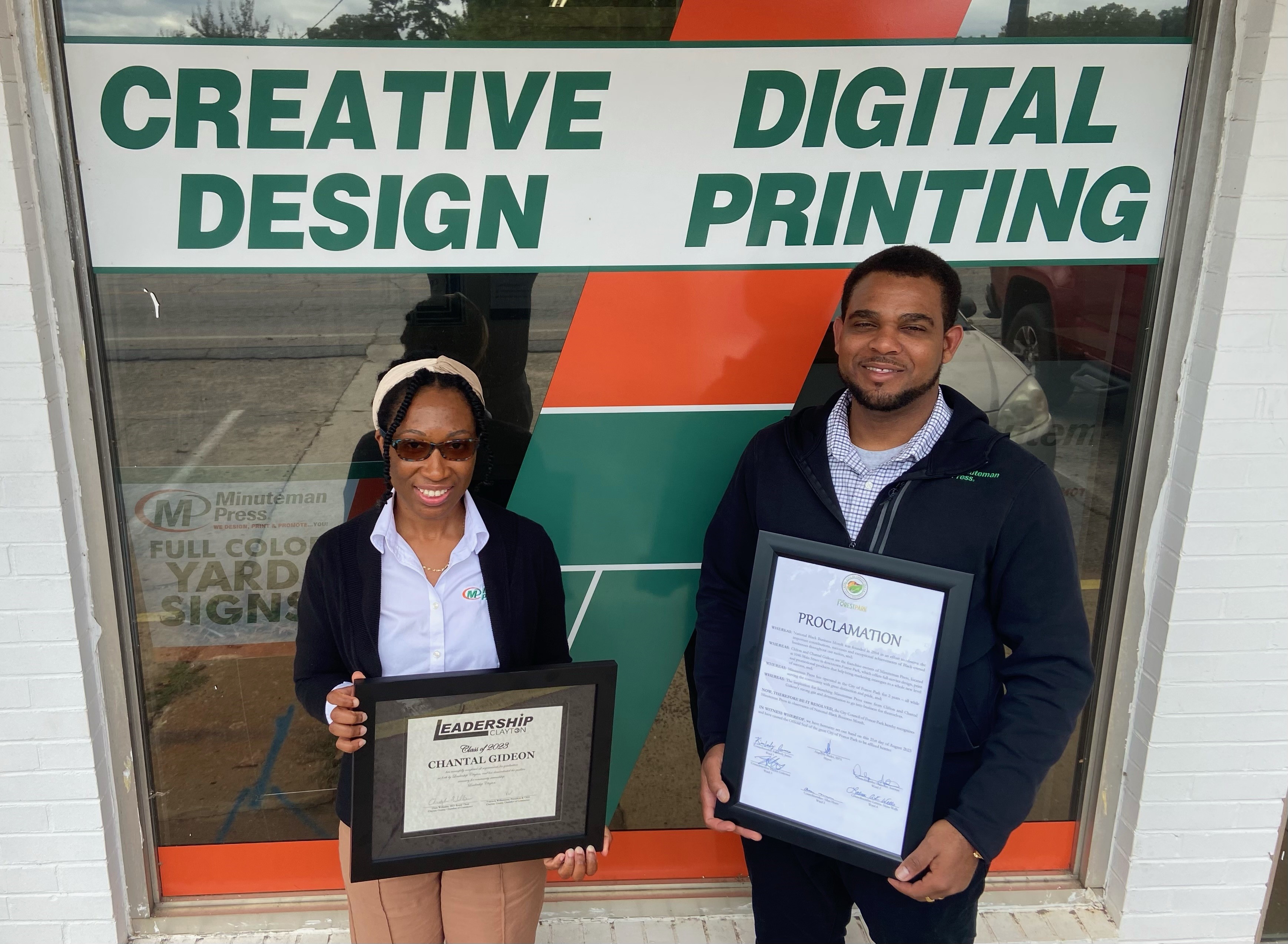Minuteman Press franchise owners Chantal &amp; Clifton Gideon with their well-earned community awards outside their business in Forest Park, GA.