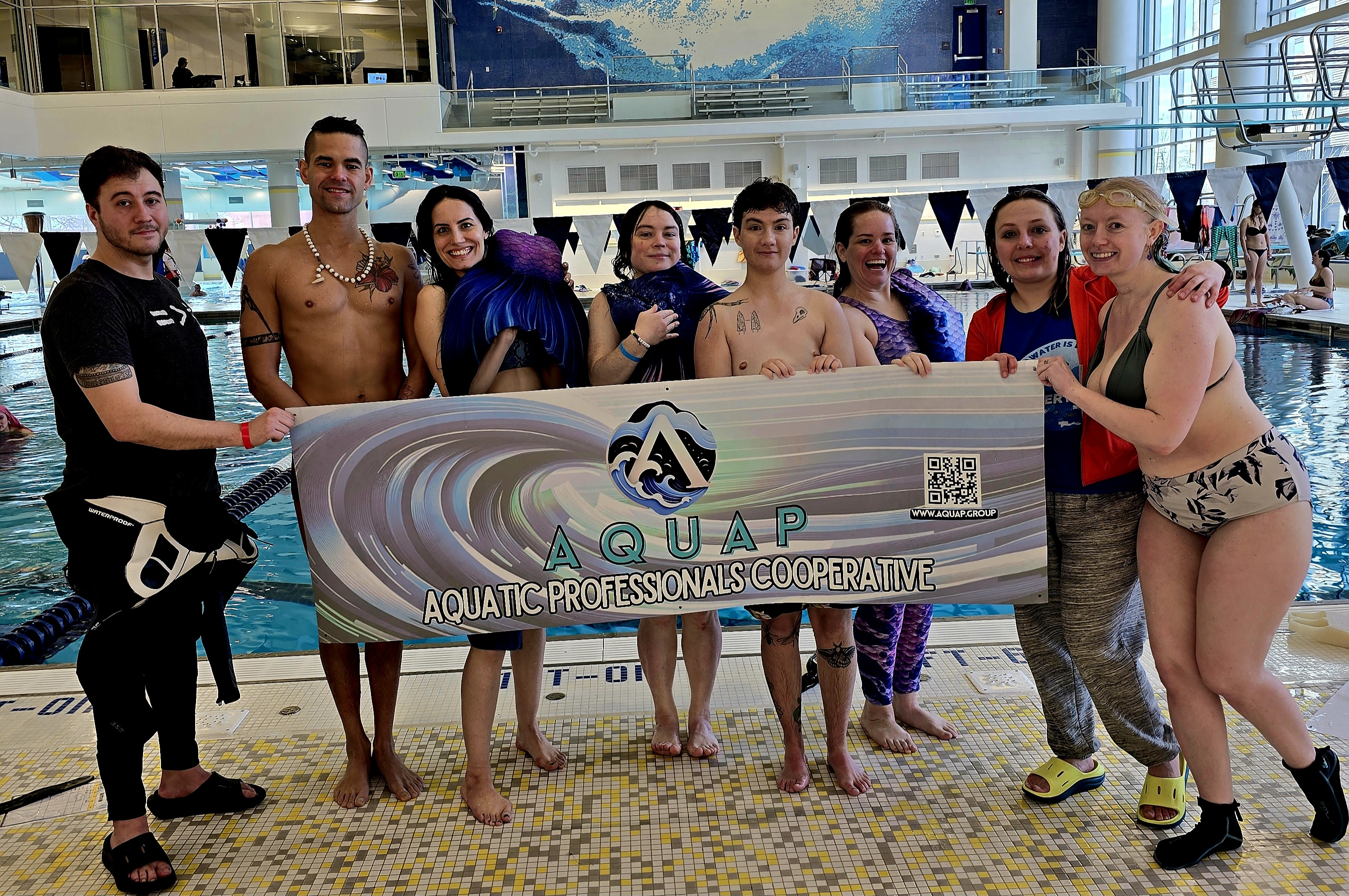 Successful mermaid certification recipients hold up the Aquap banner